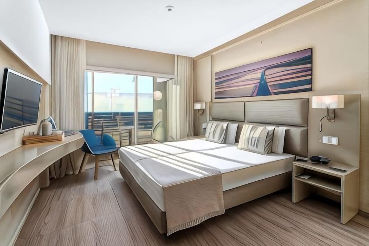 Une chambre d’hôtel avec un grand lit, un bureau, une chaise, une télévision et un tableau au mur.