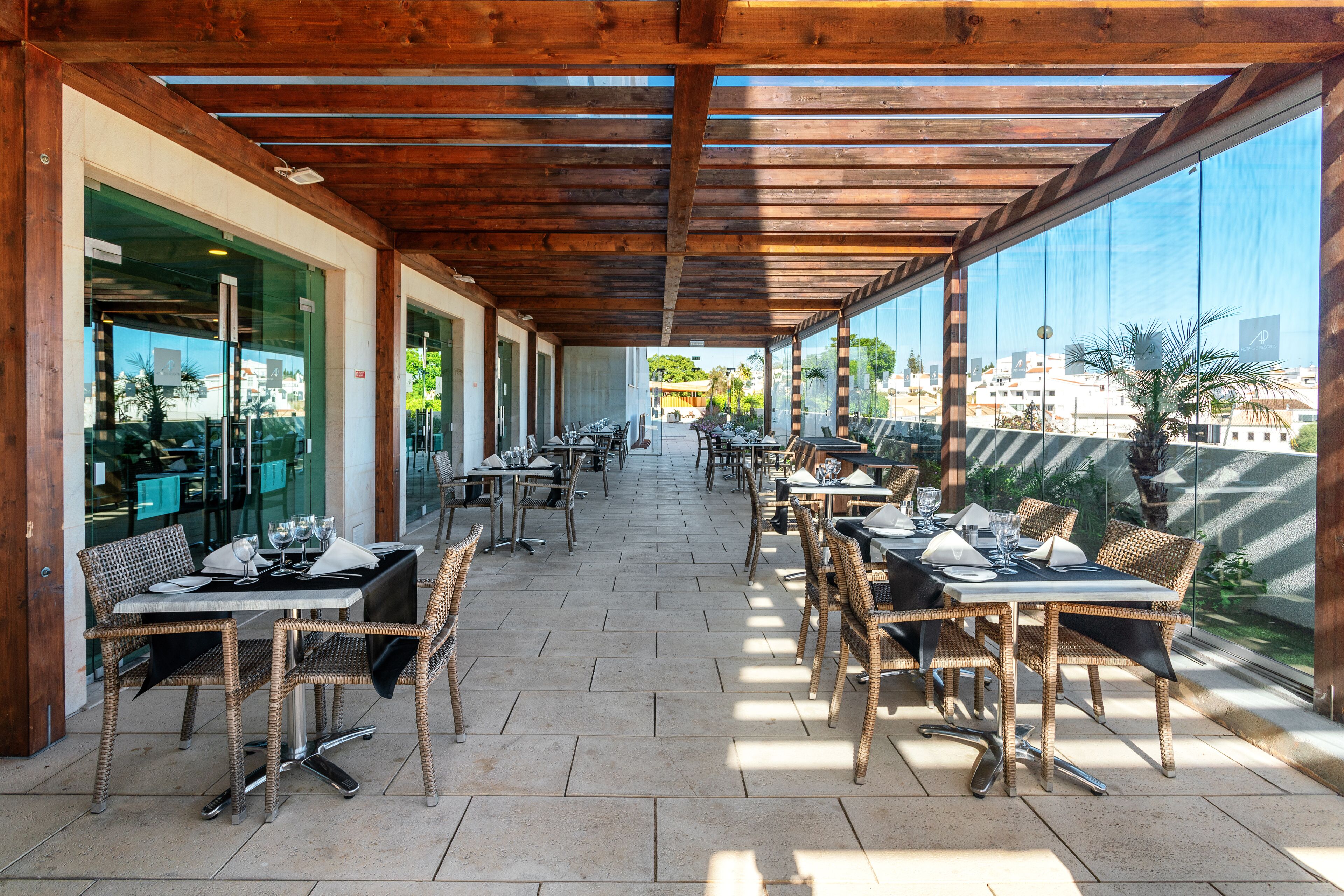 Une terrasse extérieure aménagée avec des meubles en osier et des portes vitrées donnant accès à un restaurant.