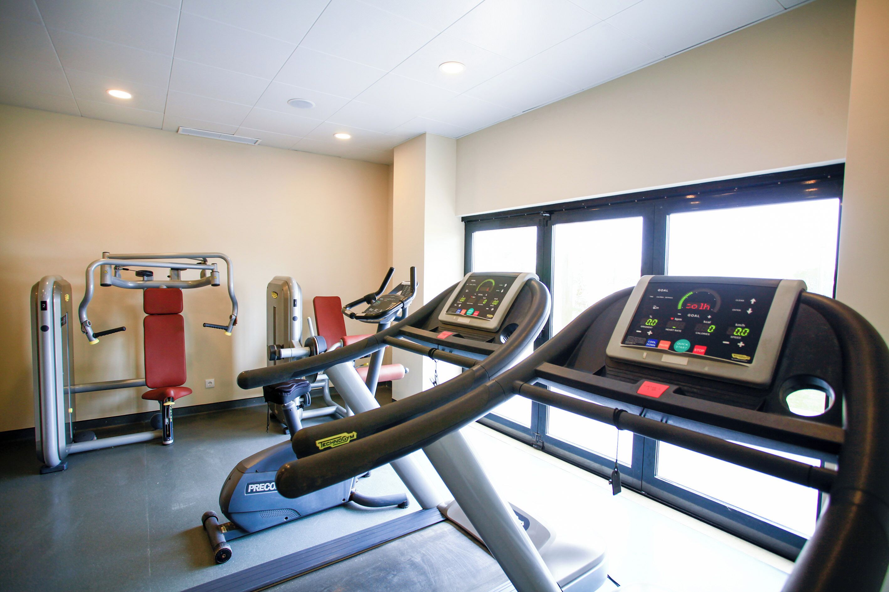 Une salle de sport équipée de matériel d’exercice, d’un tapis de course et d’une fenêtre laissant entrer la lumière naturelle.