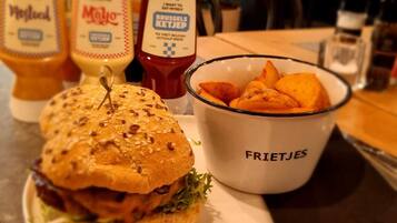 Un plato con una hamburguesa, papas fritas y kétchup, con condimentos etiquetados como 'Mayo' y 'Ketchup de Bruselas' sobre una mesa.