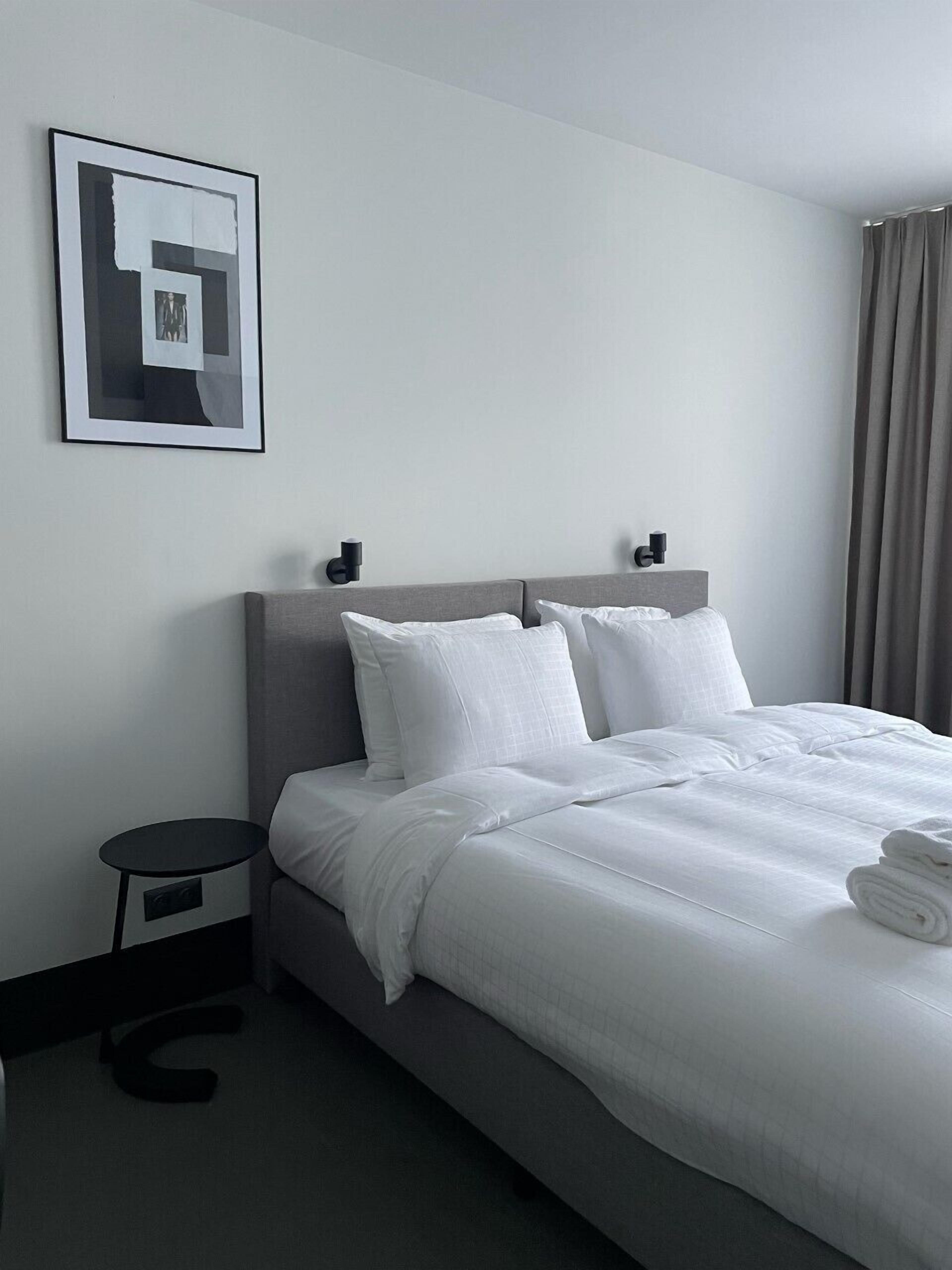 A modern hotel room with a neatly made bed, a small side table, and a framed picture on the wall.
