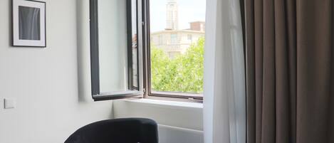 A hotel room with a single black chair, a framed picture on the wall, and a window with curtains.