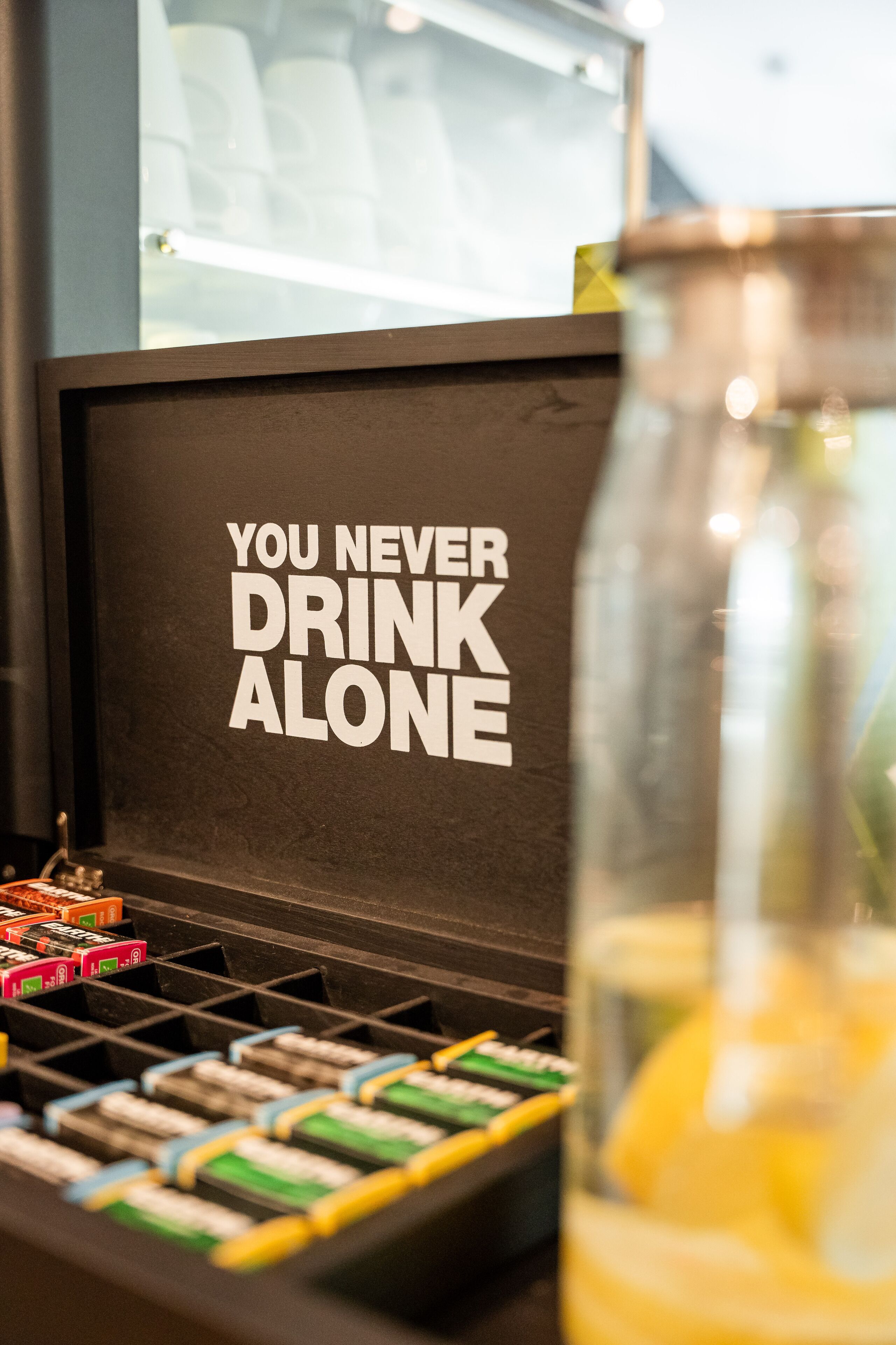 Ein Getränkespender mit einem motivierenden Schild, das "DU BIST NIEMALS ALLEIN beim Trinken" sagt, und ein Glas mit einem Zitronenscheibe.