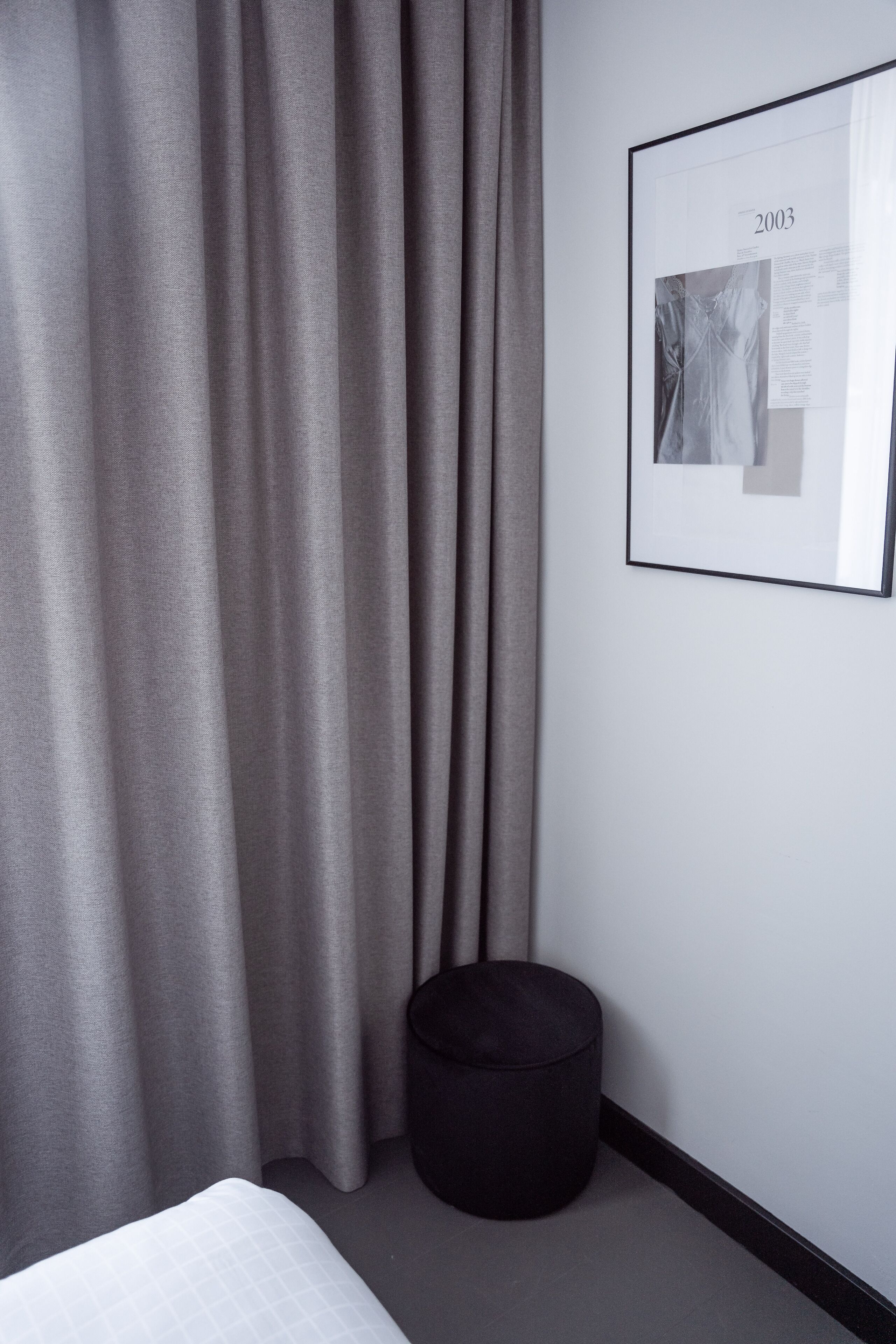 A modern hotel room with a neatly made bed, a black ottoman, and a framed picture on the wall.