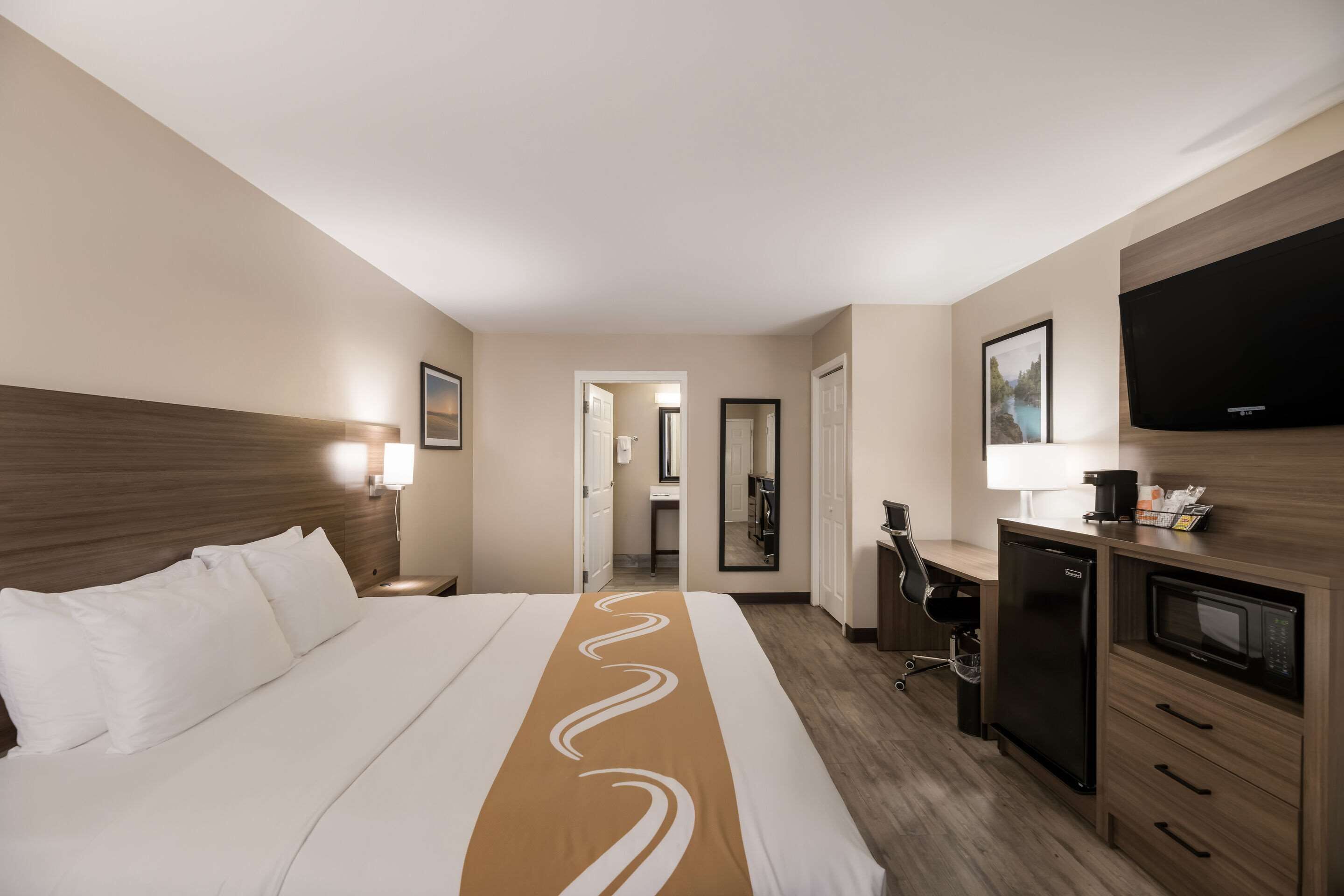 Une chambre d’hôtel avec un grand lit, un bureau, une télévision, un four à micro-ondes et un miroir.