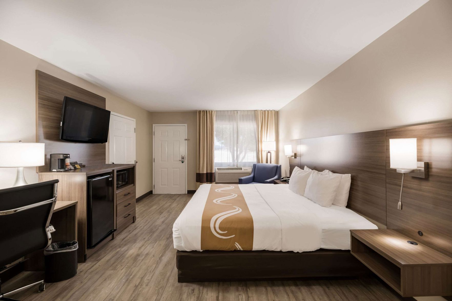 A hotel room with a bed, desk, chair, TV, and a view of the outdoors.
