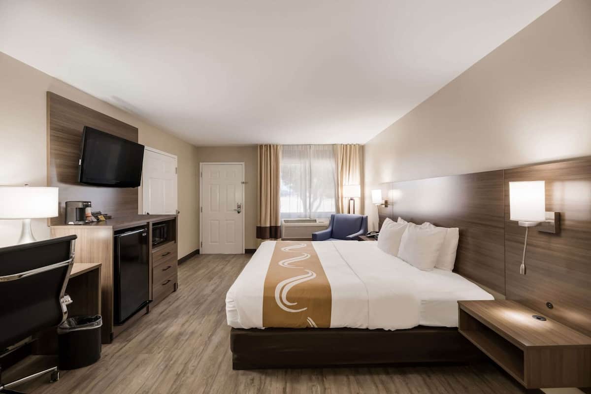 Quarto de hotel com cama, escrivaninha, cadeira, televisão e vista para o exterior.