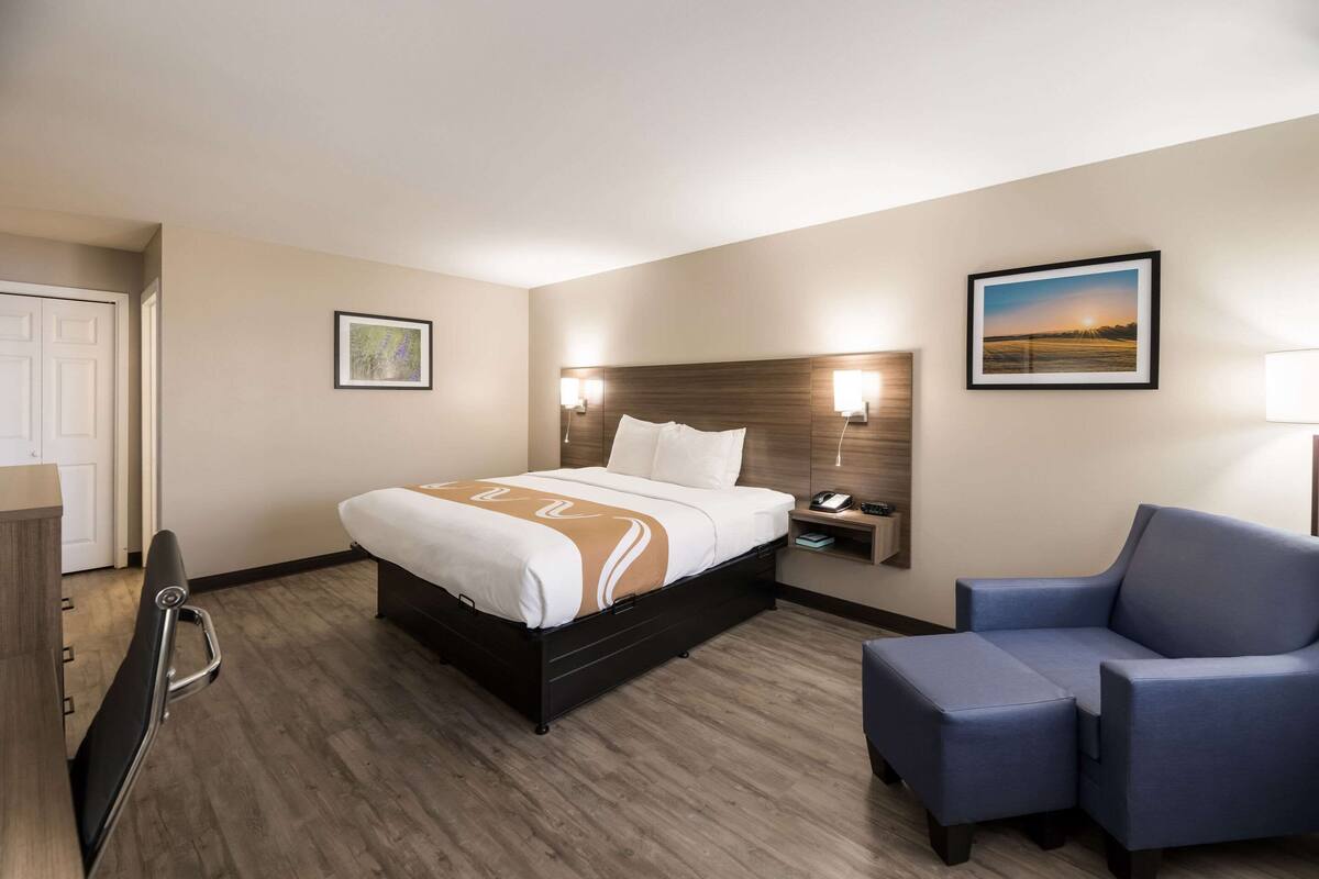 Quarto de hotel com cama, mesa de cabeceira, cadeira e um quadro na parede.