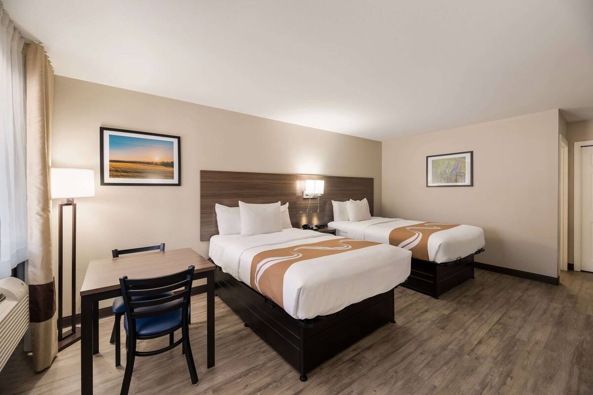 Quarto de hotel com duas camas, uma escrivaninha e cadeiras.