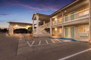 A multi-story hotel with a covered entrance, outdoor seating area, and a parking lot with handicapped accessibility.