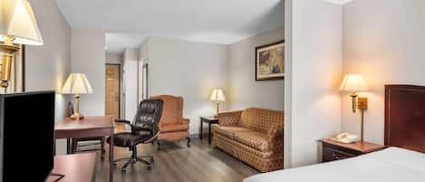 A hotel room with a bed, desk, two chairs, a sofa, and a TV.