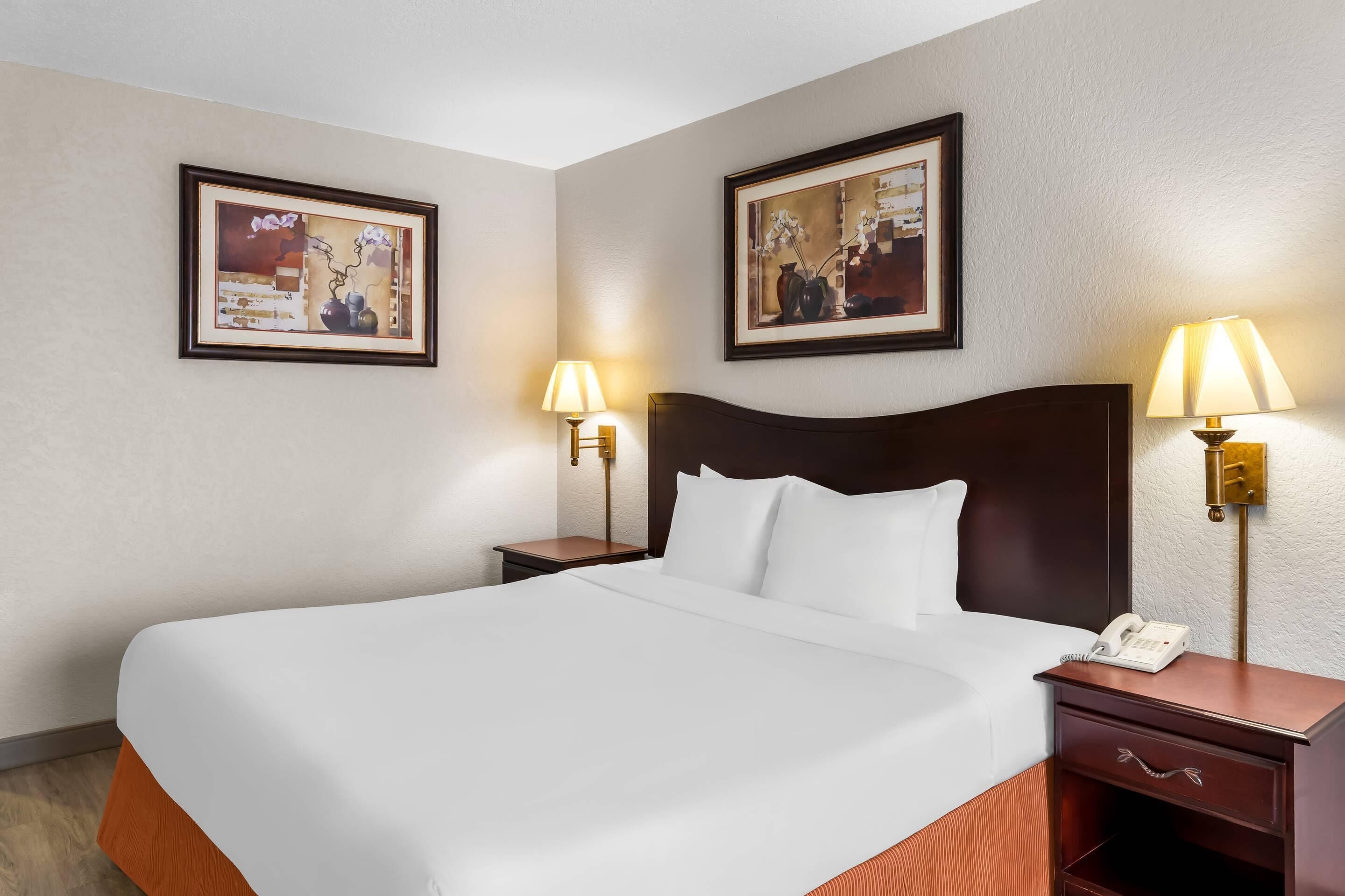 A hotel room with a large bed, two bedside tables with lamps, and two framed pictures on the wall.