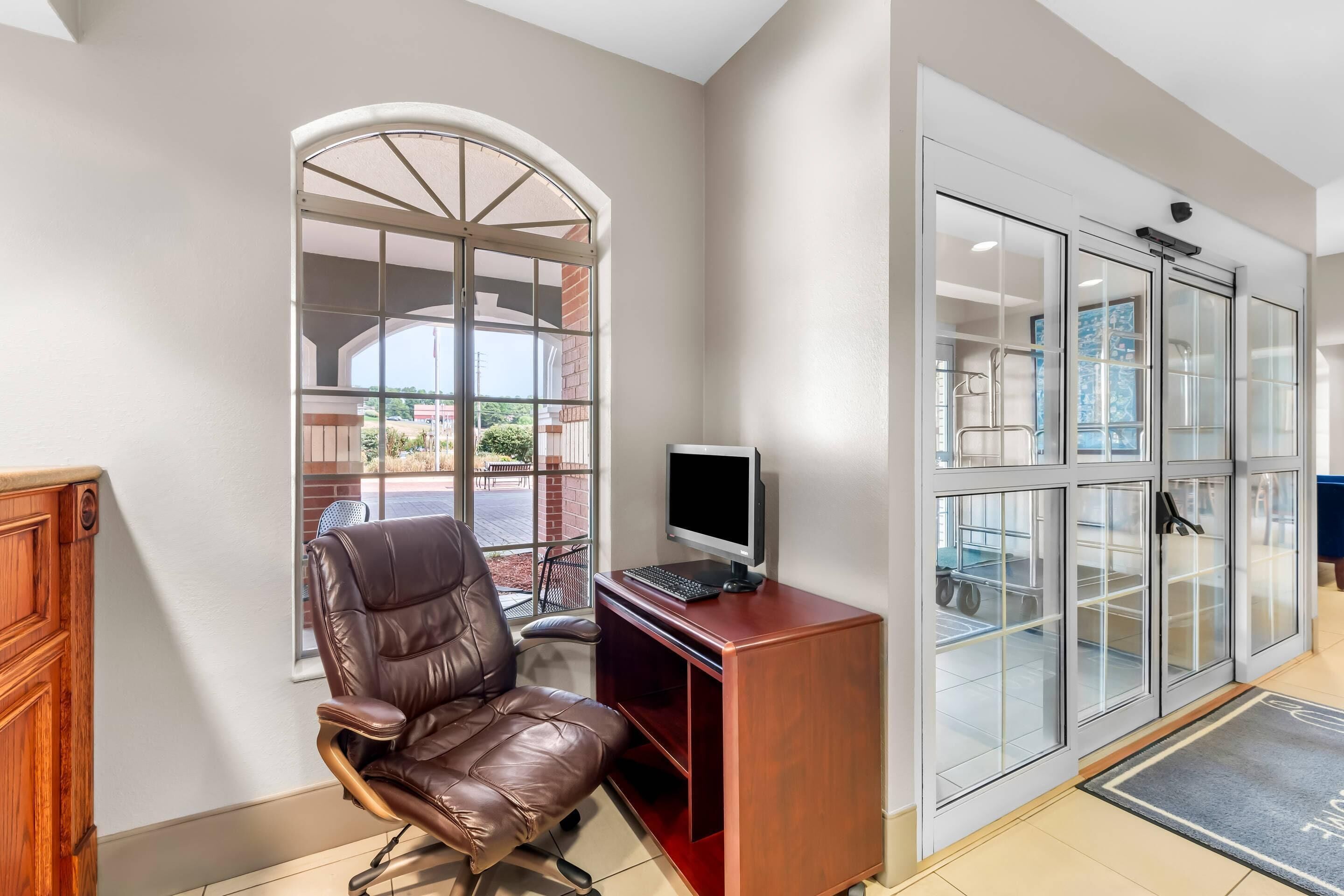 A room with a leather chair, a desk with a computer, a large window, and a glass door leading to a storage area.