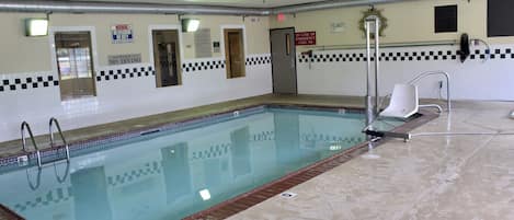 En inomhuspool med ett rutmönstrat kakel runt kanten, en livräddarstol och en skylt som förbjuder dykning.
