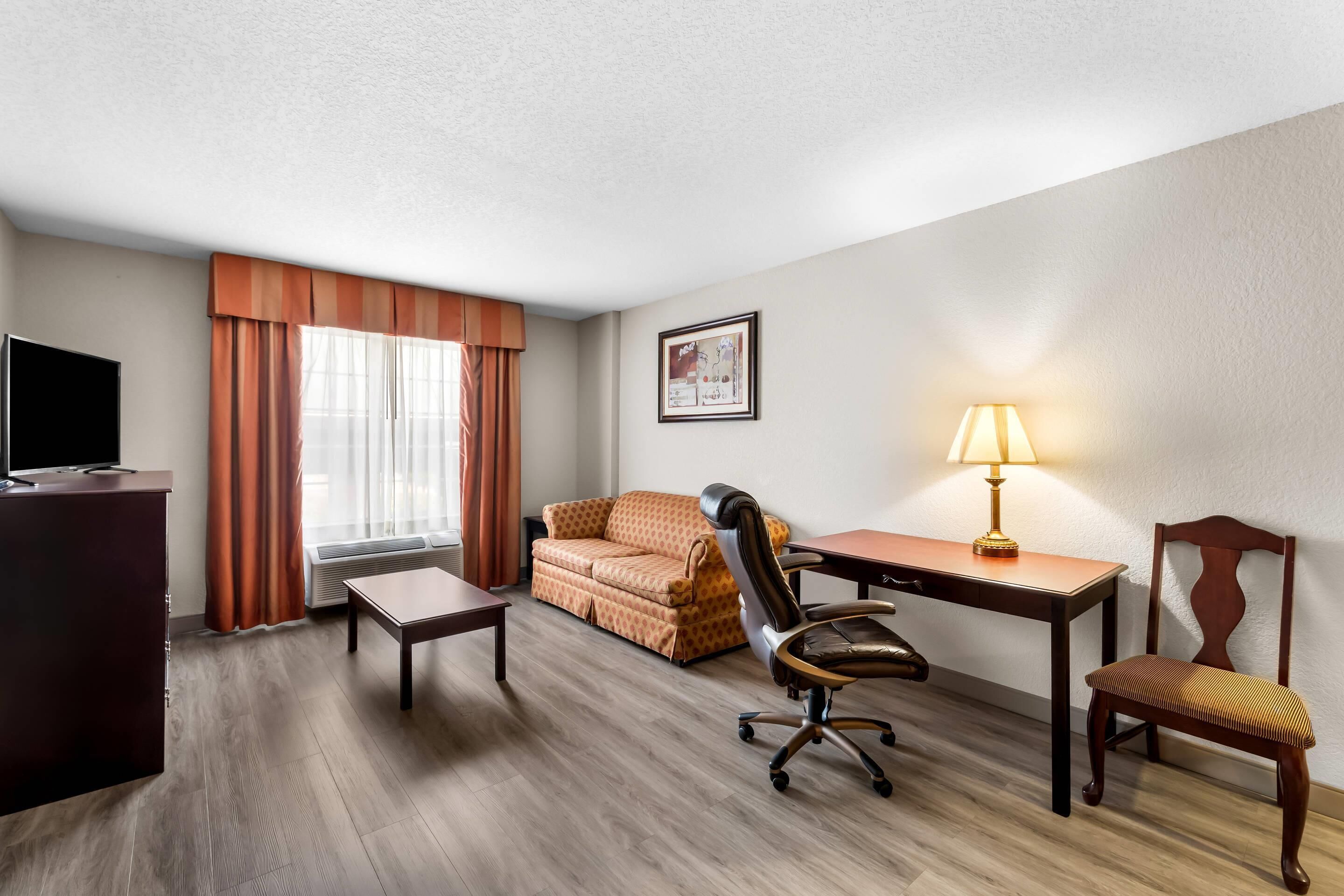 Une chambre d’hôtel avec un plancher en bois, un canapé, un bureau avec une lampe, une télévision et un tableau encadré au mur.