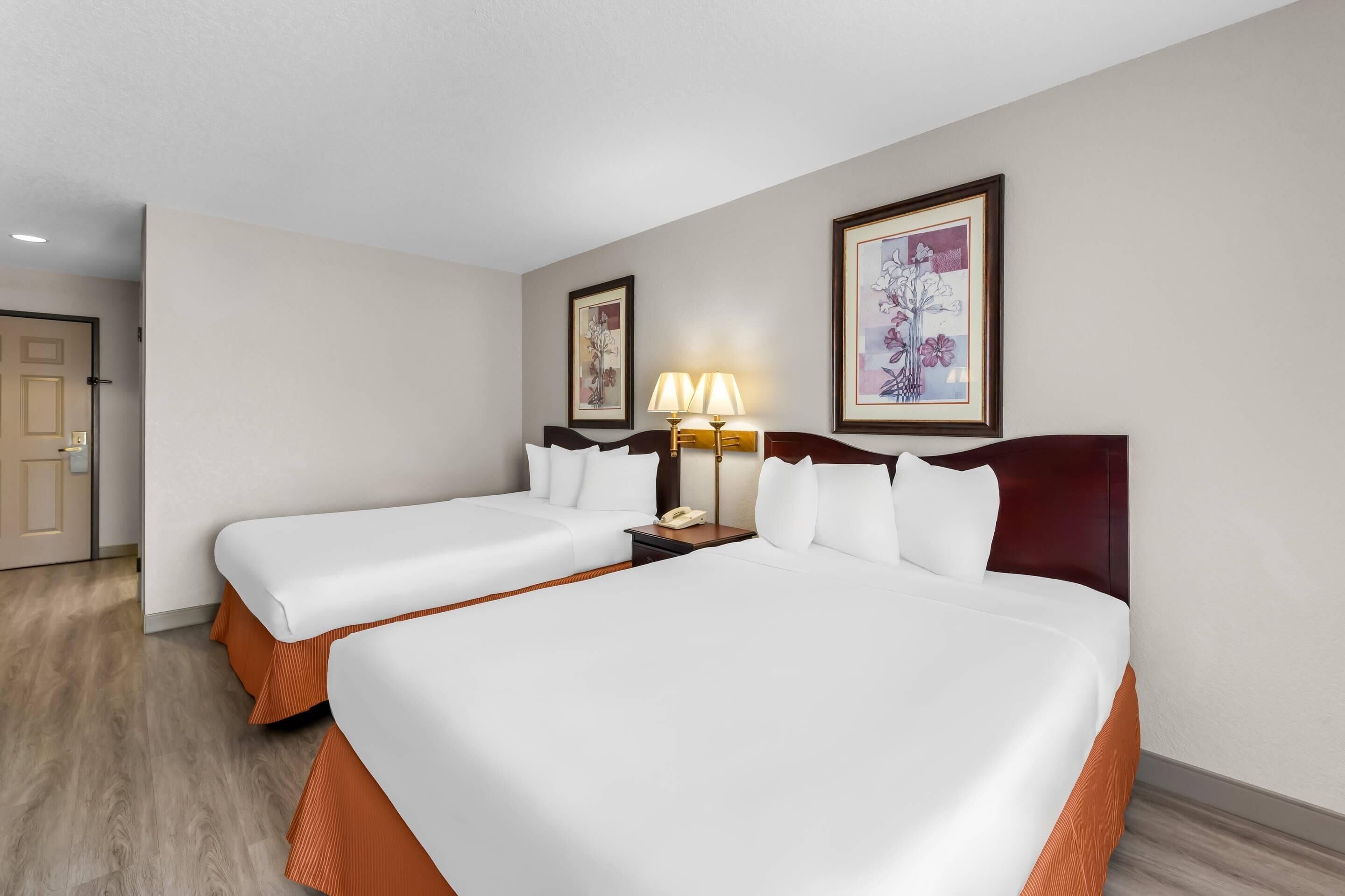 A hotel room with two beds, a nightstand with a lamp, and framed artwork on the walls.