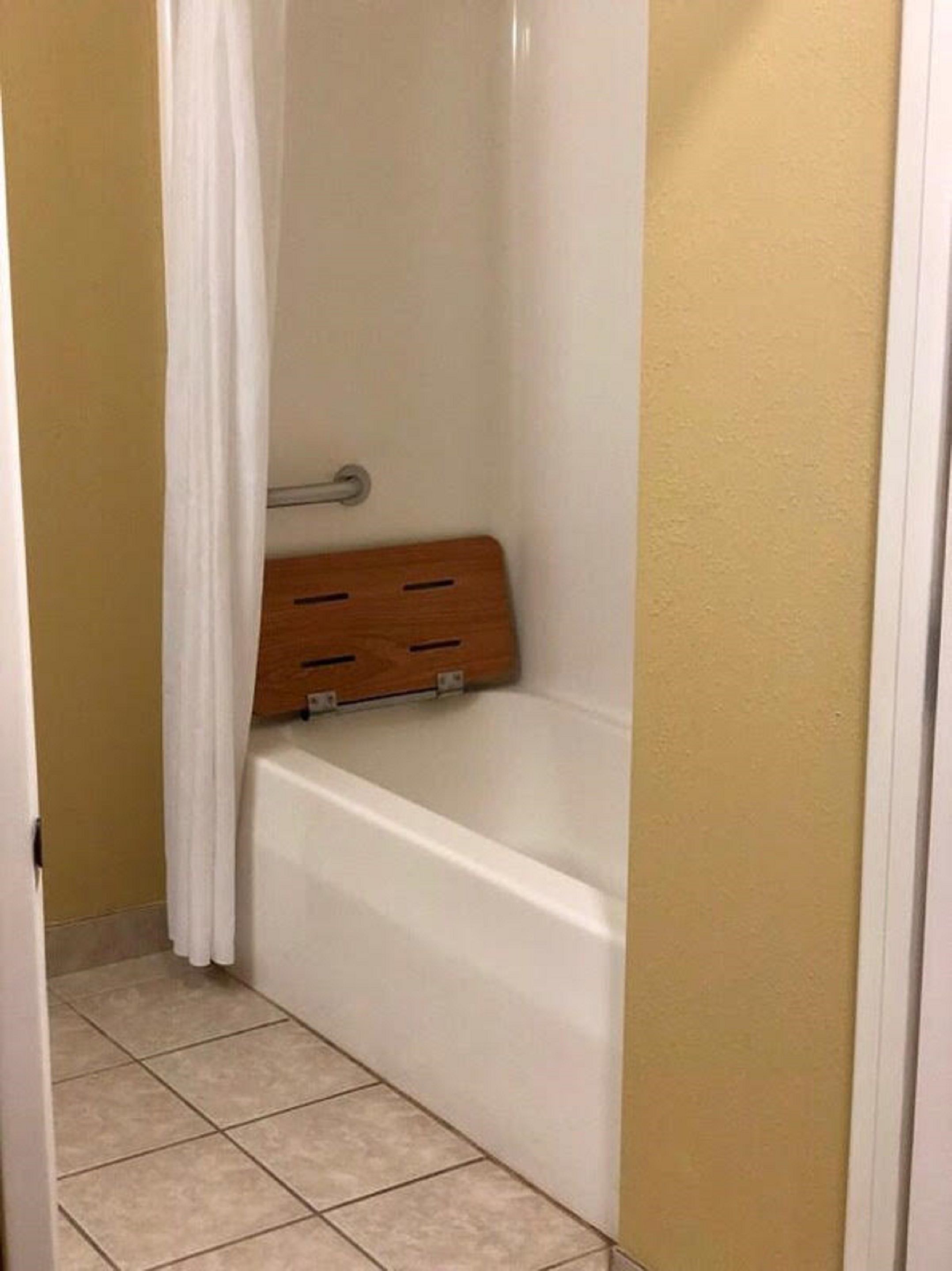 A bathroom with a white bathtub, a wooden shelf, and a white curtain.
