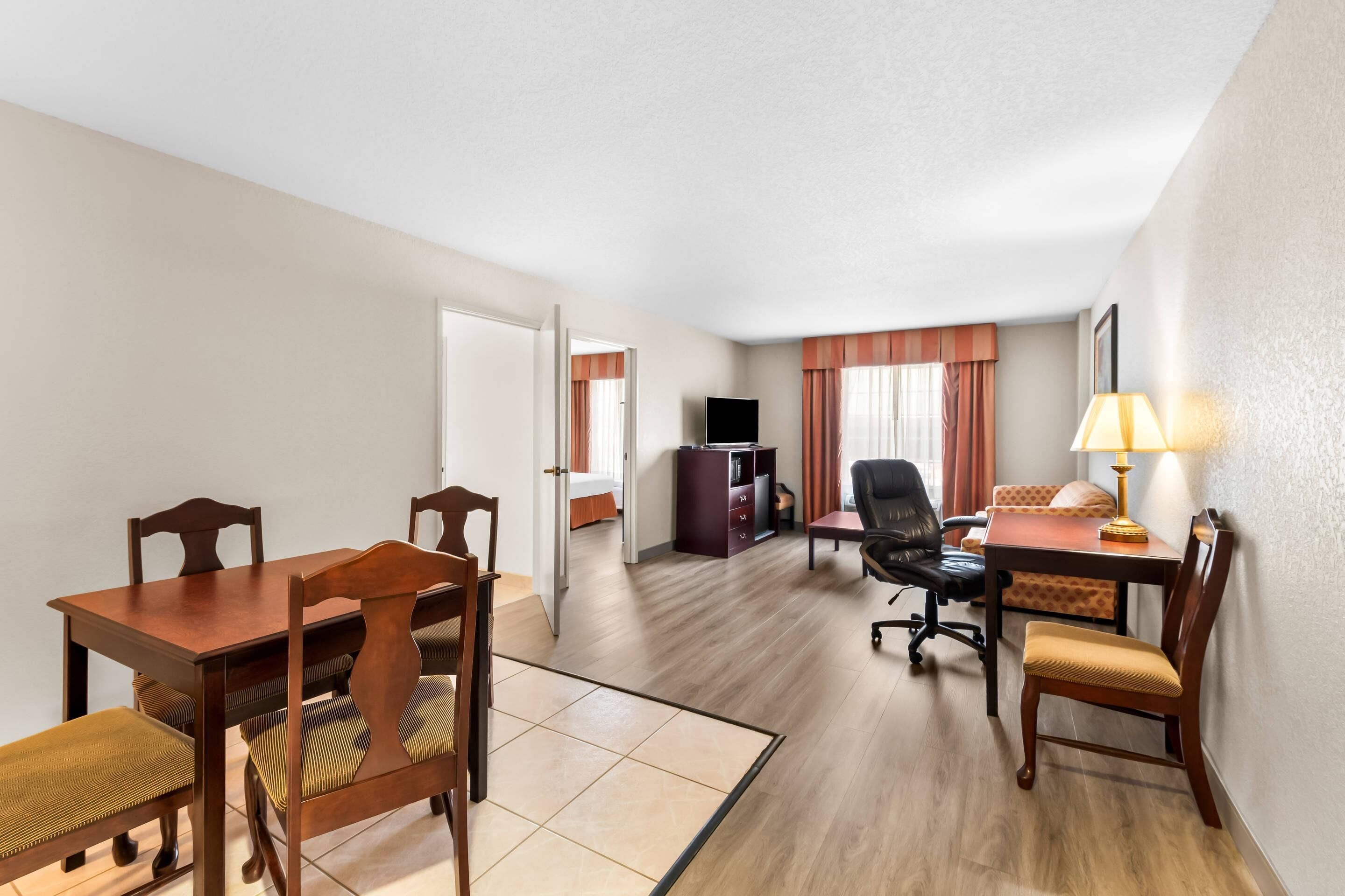 Une chambre d’hôtel équipée d’une table à manger, de chaises, d’un téléviseur, d’un bureau et d’une lampe.