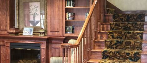 Un magnifique escalier orné de sculptures, une cheminée agrémentée d’un tableau encadré et une bibliothèque remplie de livres.