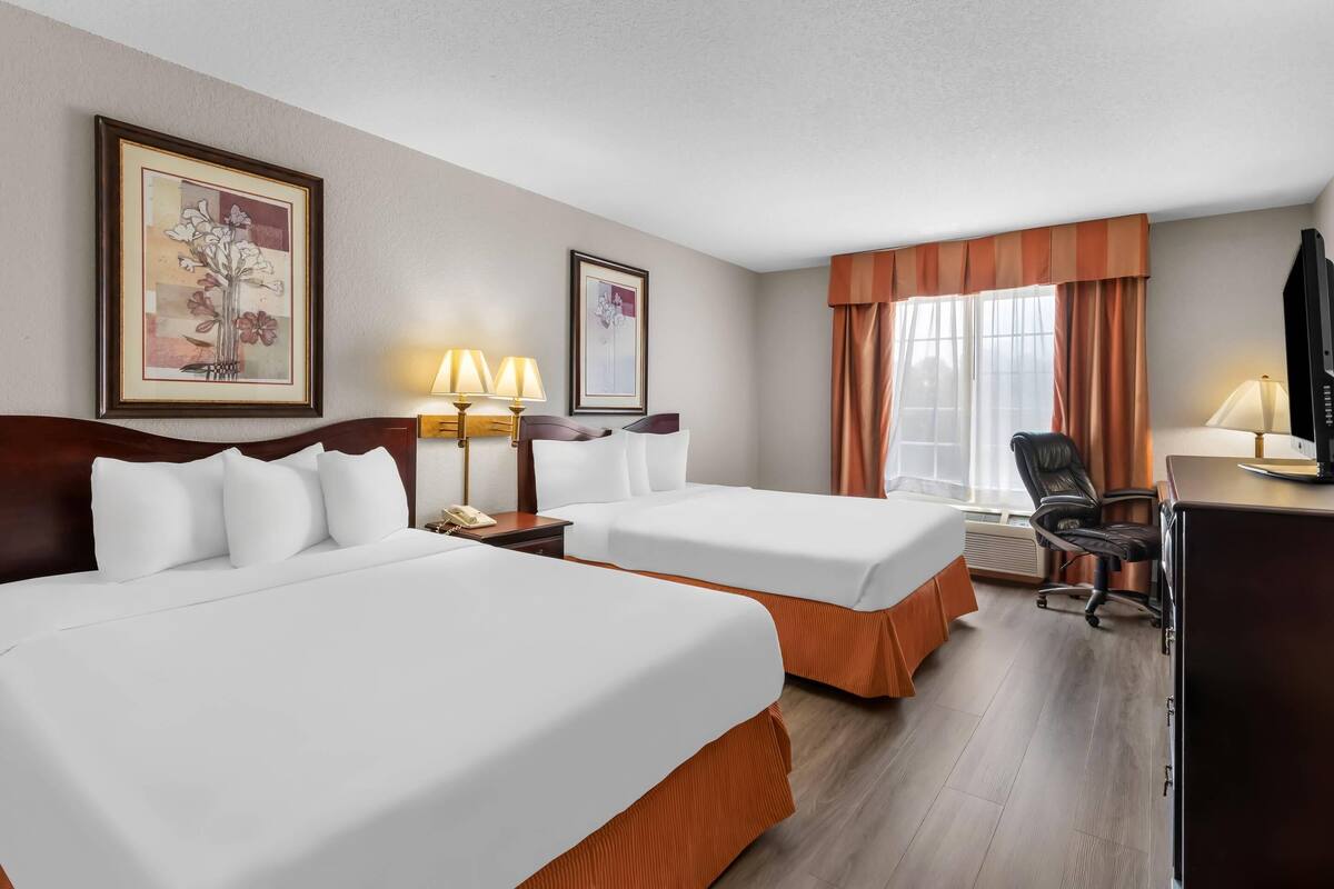A hotel room with two beds, a desk, a chair, and two lamps.