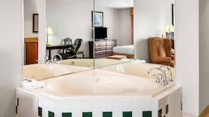 A hotel bathroom with a large mirror, a bathtub, a sink, a chair, and a desk with a television. - Country Inn & Suites by Radisson, Hot Springs, AR (Hot Springs)