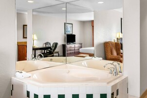 Un baño de hotel con un espejo grande, una bañera, un lavabo, una silla y un escritorio con televisor.