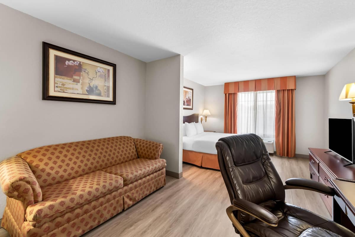 A hotel room with a sofa, a leather chair, a bed, a desk, and a television.