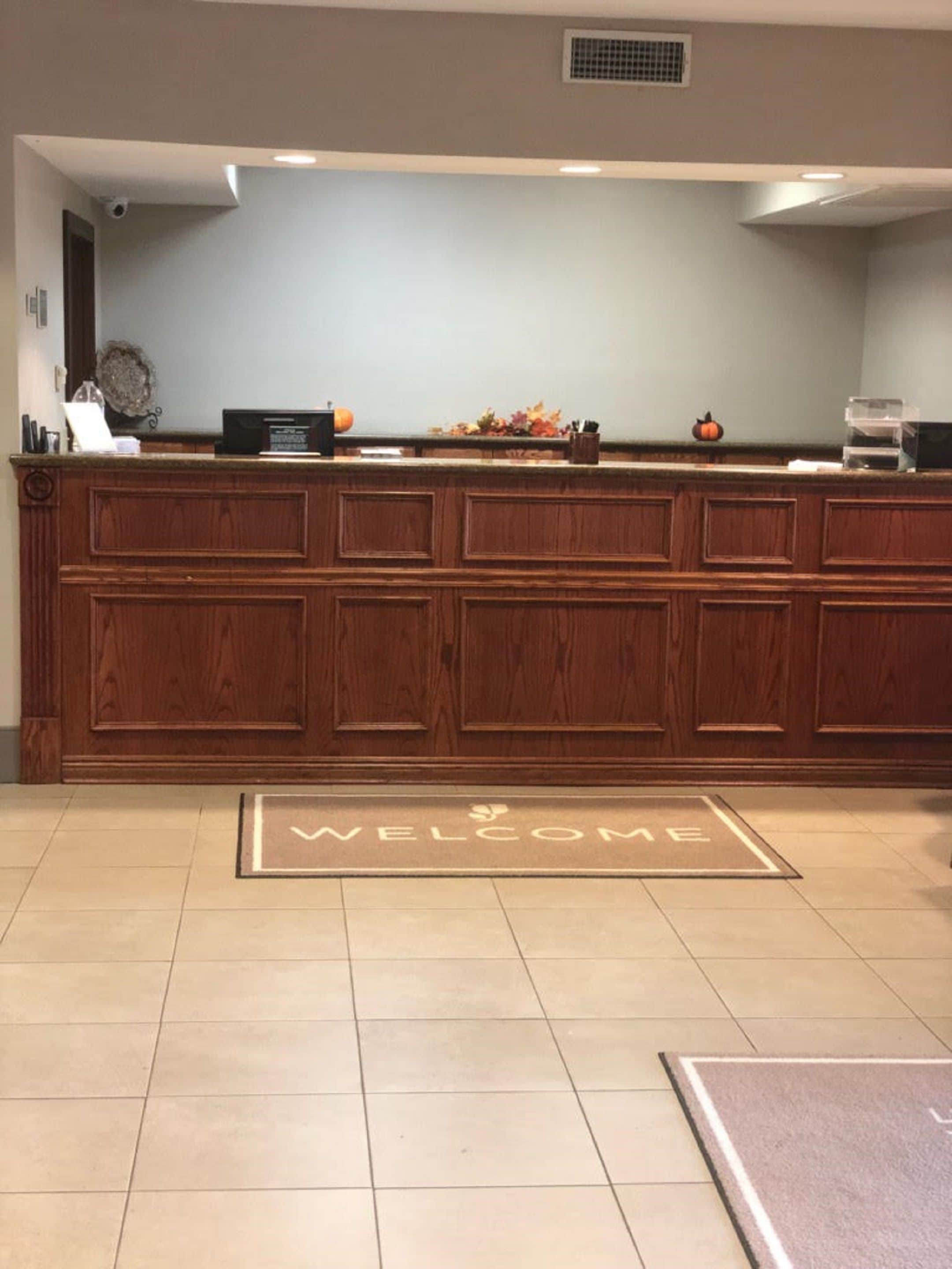 A reception area with a wooden reception desk, a welcome mat, and a wall-mounted security camera.