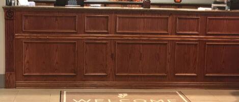 A reception area with a wooden reception desk, a welcome mat, and a wall-mounted security camera.