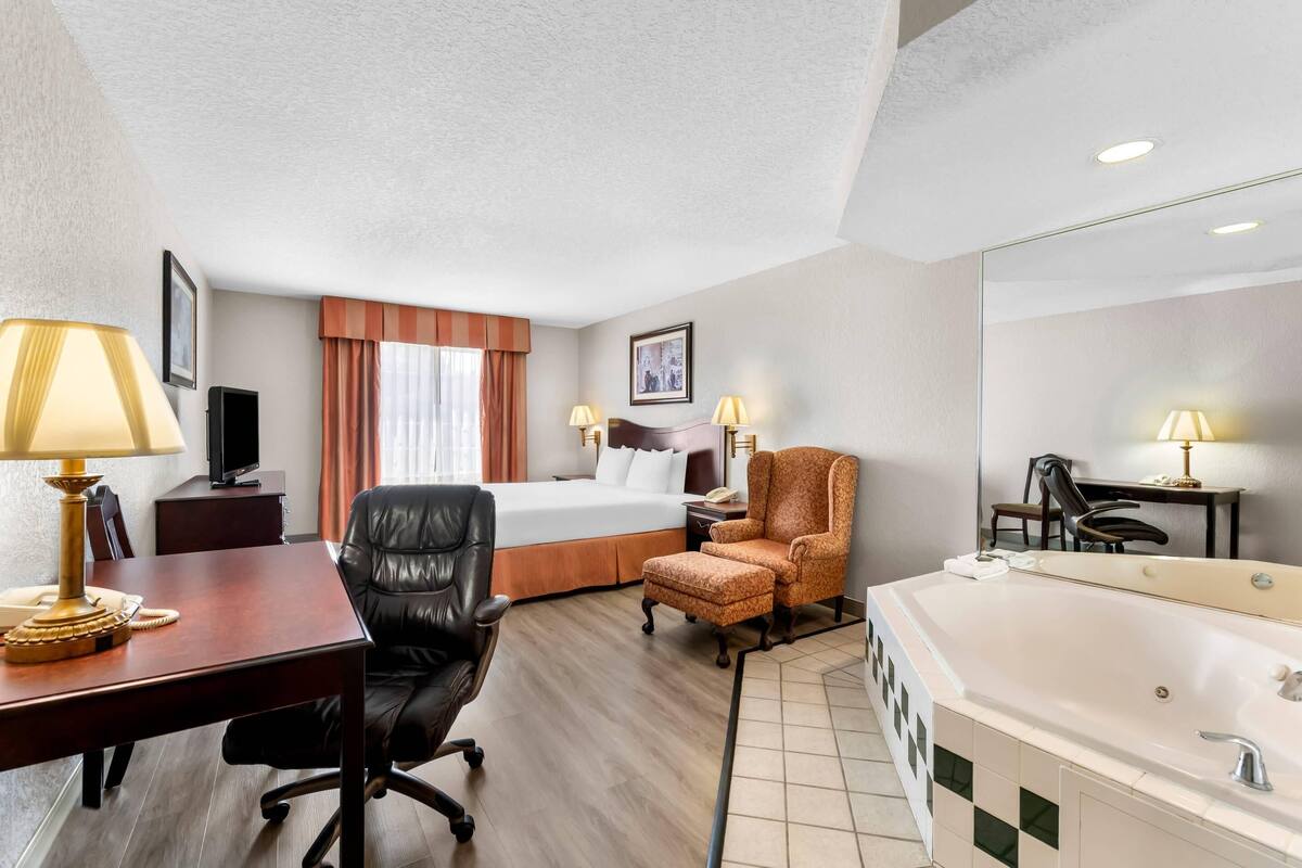 A hotel room with a bed, desk, office chair, armchair, and a large bathtub.