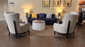 Ein modernes Wohnzimmer mit einem dunkelblauen Sofa, zwei grauen Sessel und einem runden Couchtisch, sowie drei Wandleuchten.
