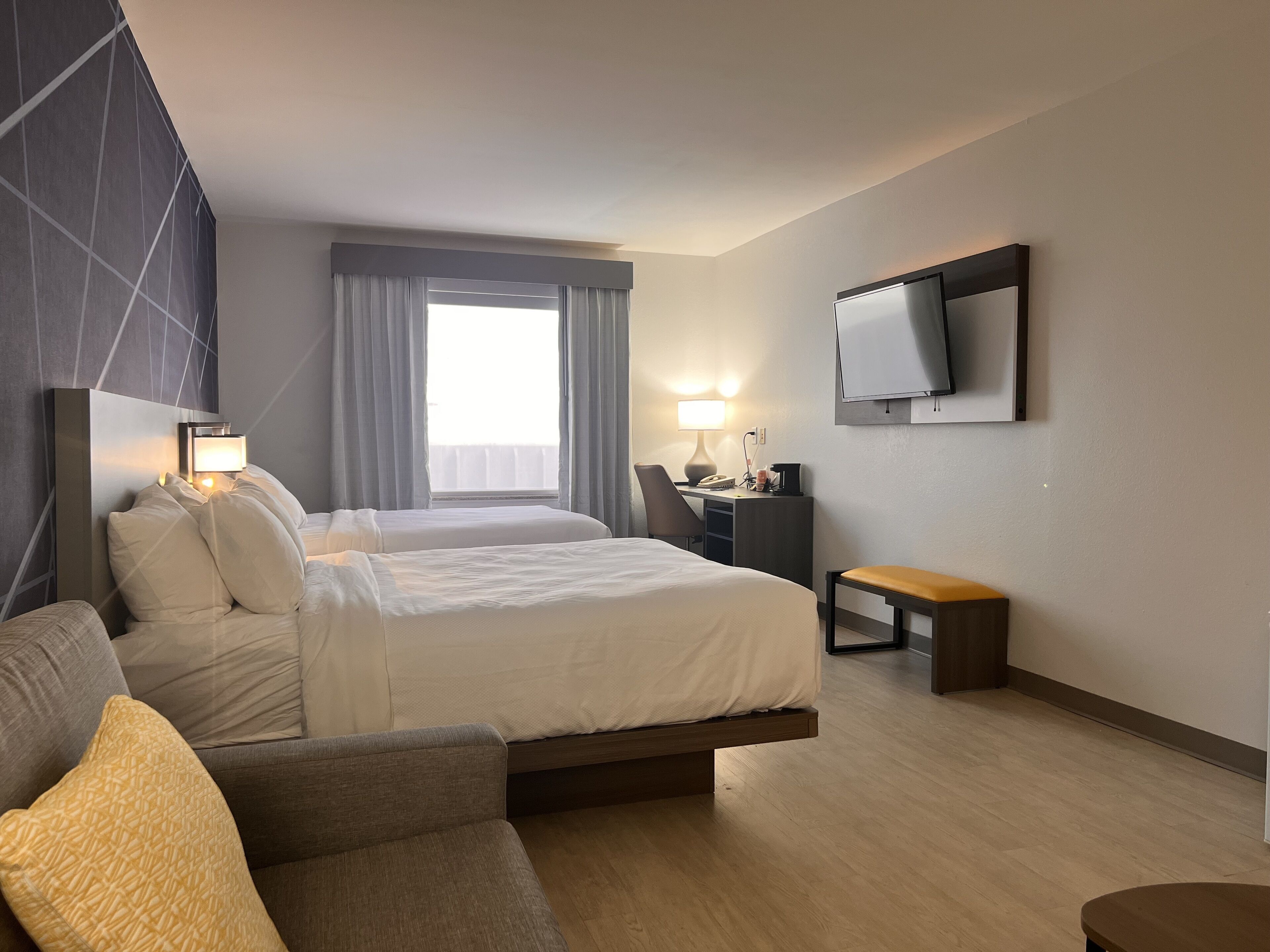 Een hotelkamer met een bed, een bureau, een stoel, een televisie en een raam met gordijnen.