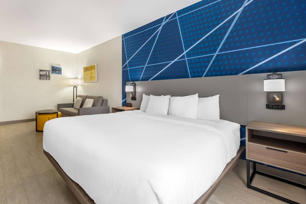 Ein Hotelzimmer mit einem großen Bett, einer Couch, einem Schreibtisch und einer Wand mit geometrischem Muster.