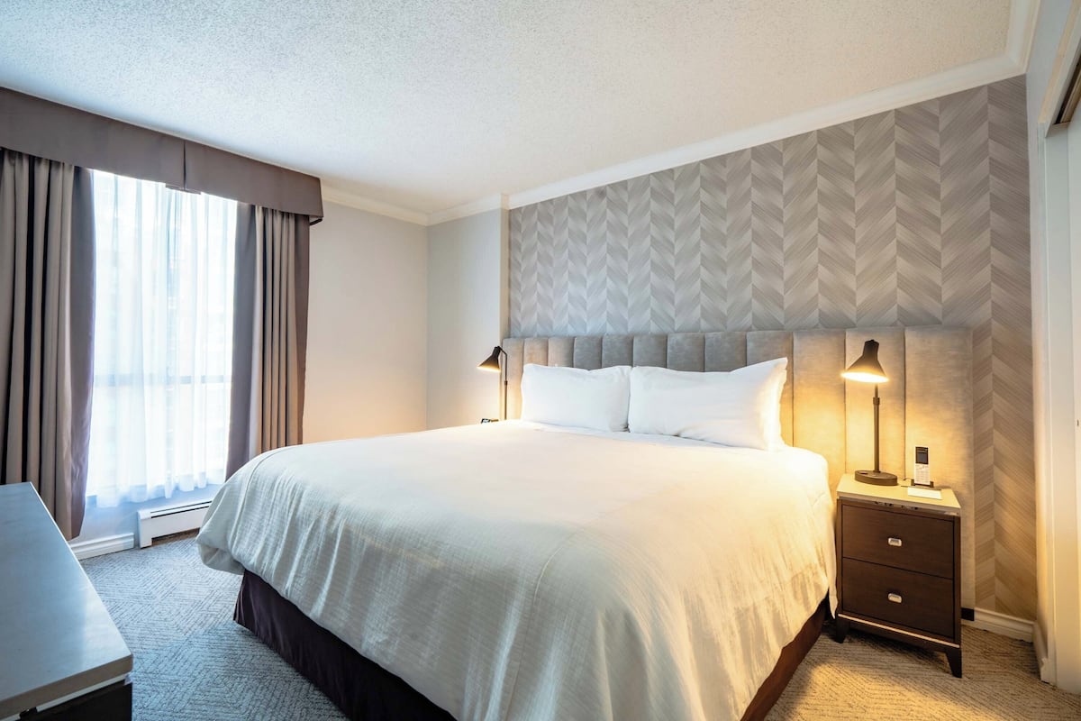 A hotel room with a large bed, bedside tables with lamps, a desk, and a view of the outdoors through the window.