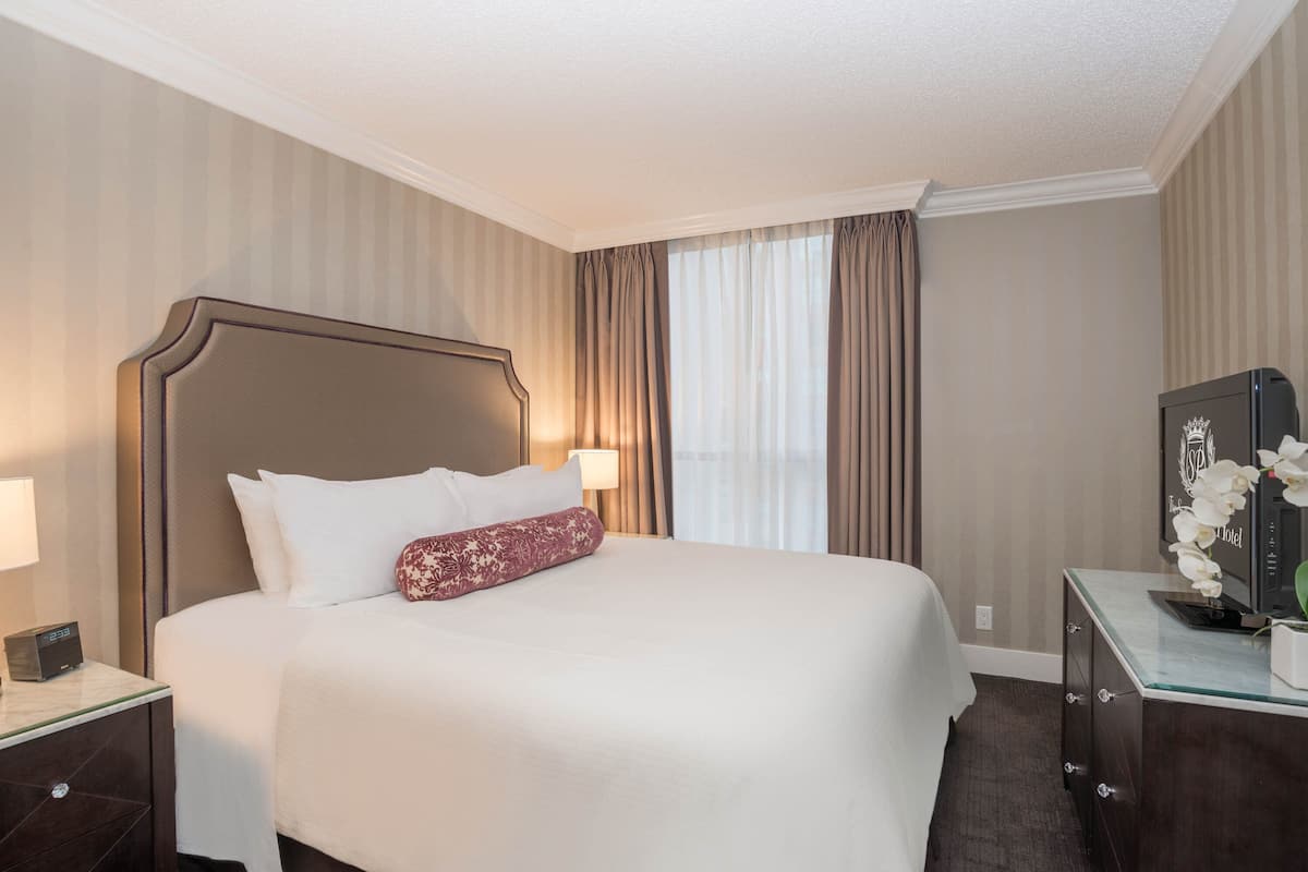 A hotel room with a large bed, a nightstand with a lamp, a dresser, and a television.
