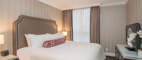 A hotel room with a large bed, a nightstand with a lamp, a dresser, and a television.