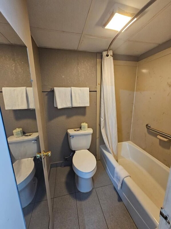 Une salle de bain avec des toilettes, un lavabo et une baignoire. Des serviettes sont accrochées au mur et il y a un rideau de douche.