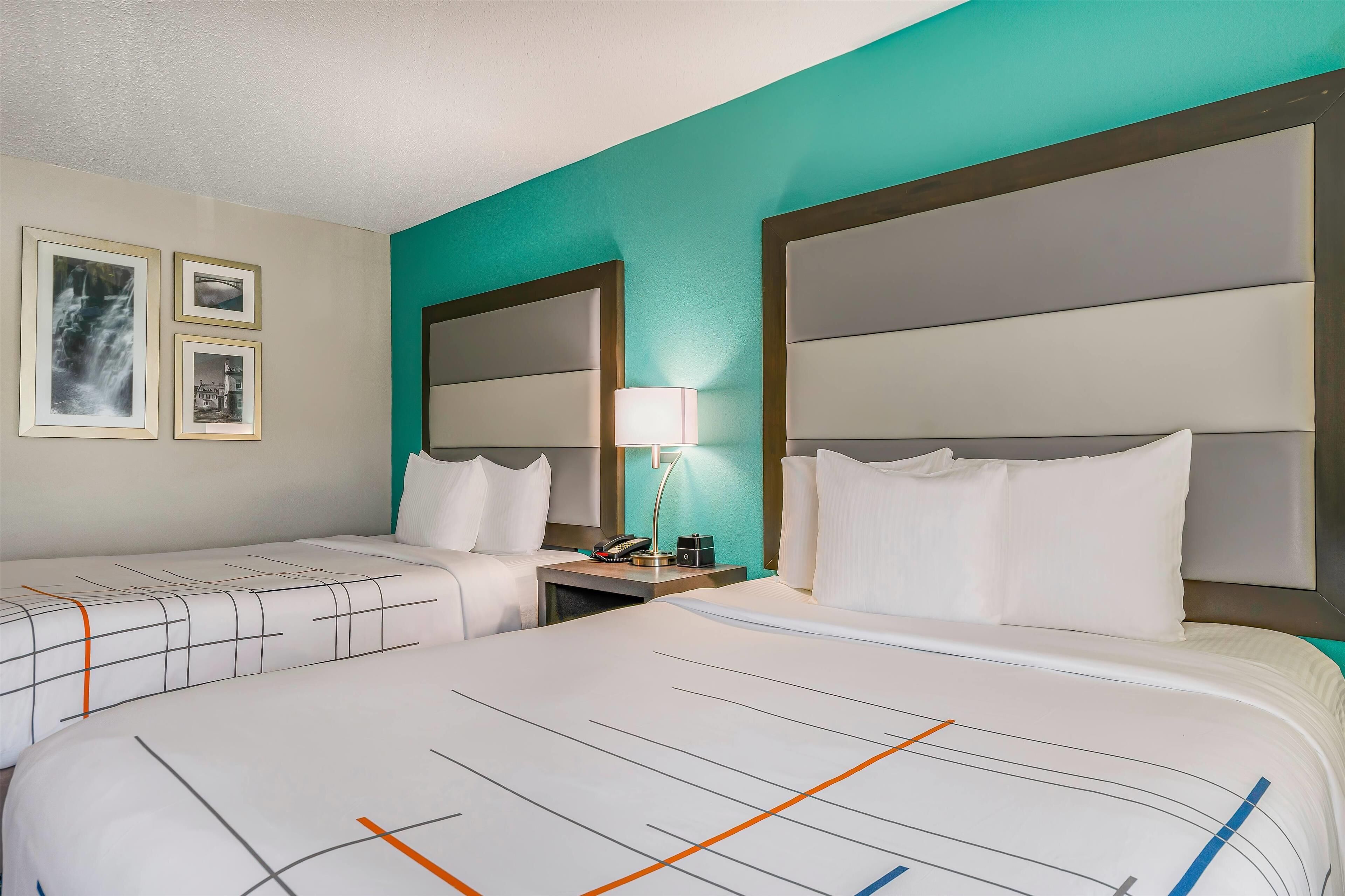 A hotel room with two beds, a nightstand with a lamp, and framed pictures on the wall.