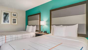 A hotel room with two beds, a nightstand with a lamp, and framed pictures on the wall.