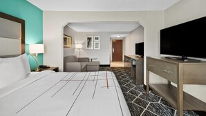 A hotel room with a bed, a desk, a television, and a bathroom visible through an archway. - La Quinta Inn & Suites by Wyndham Batavia (Batavia)