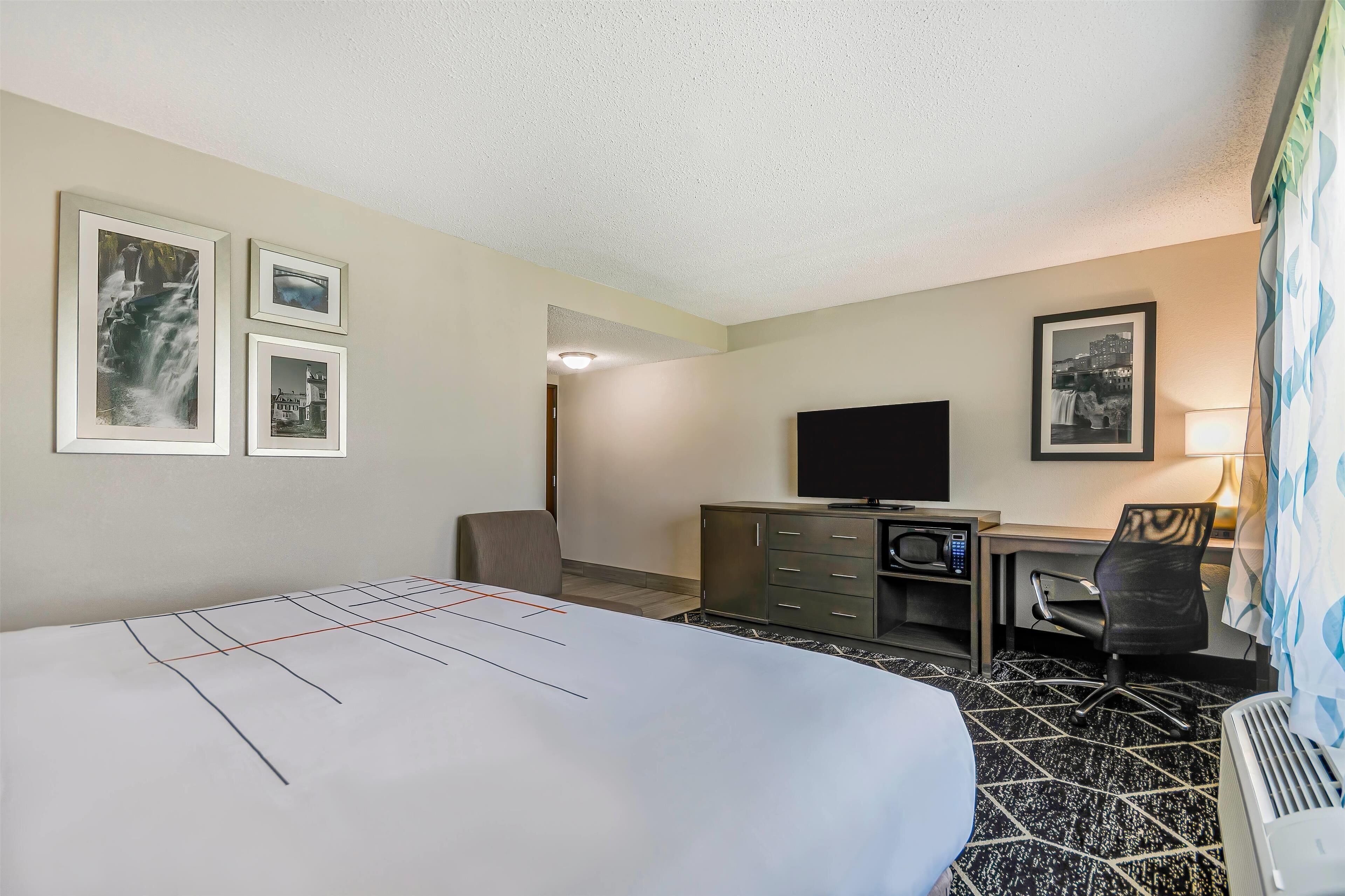 Een hotelkamer met een bed, een bureau met een computer, een televisie en ingelijste foto’s aan de muur.