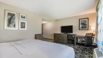 Een hotelkamer met een bed, een bureau met een computer, een televisie en ingelijste foto’s aan de muur.