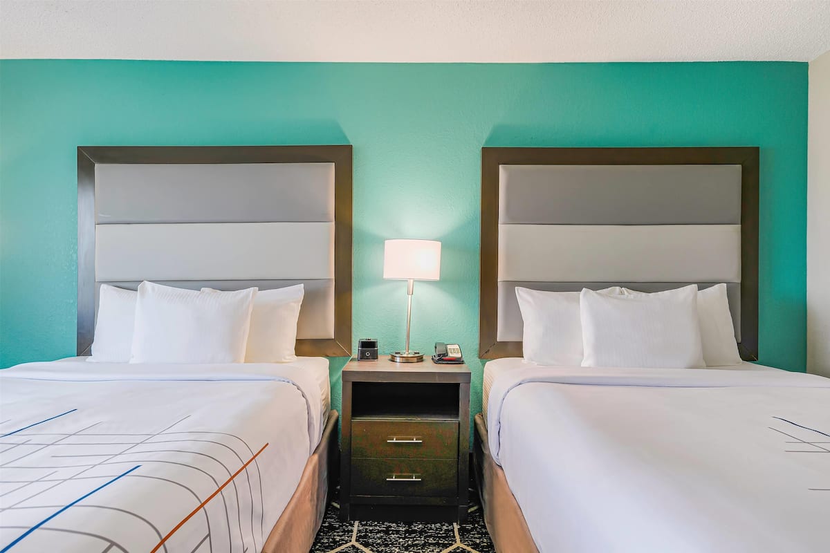 Une chambre d’hôtel avec deux lits, une table de chevet avec une lampe et un petit tiroir.