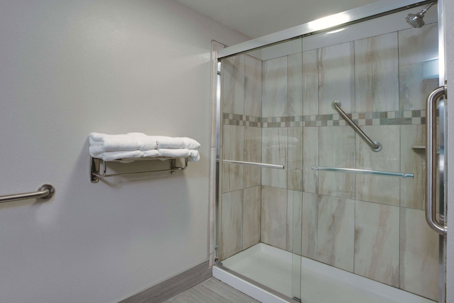 Una ducha con puertas de cristal, un perchero con toallas dobladas y un pasamanos.