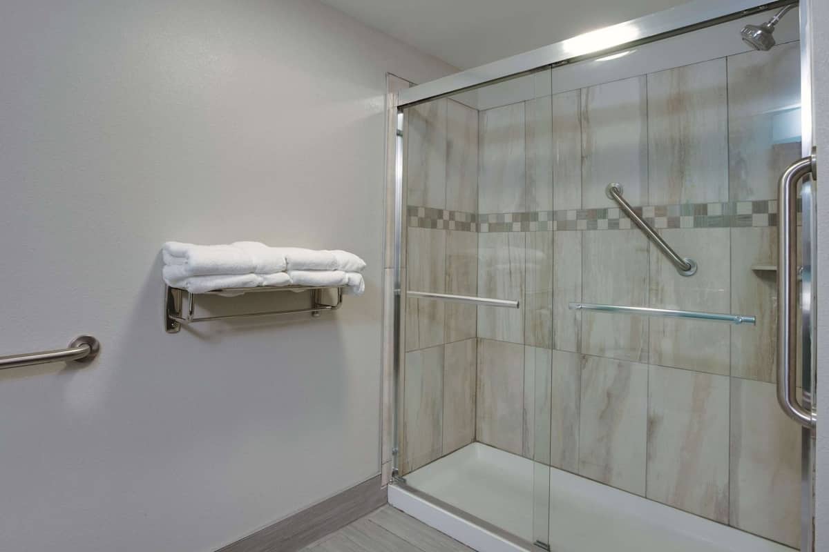 Une douche avec des portes en verre, un porte-serviettes avec des serviettes pliées et une barre d’appui.