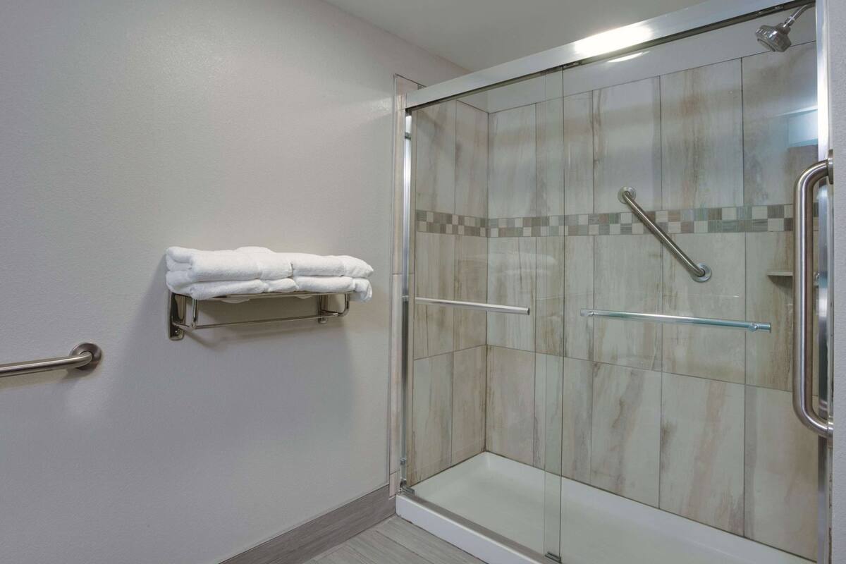 Une douche avec des portes en verre, un porte-serviettes avec des serviettes pliées et une barre d’appui.
