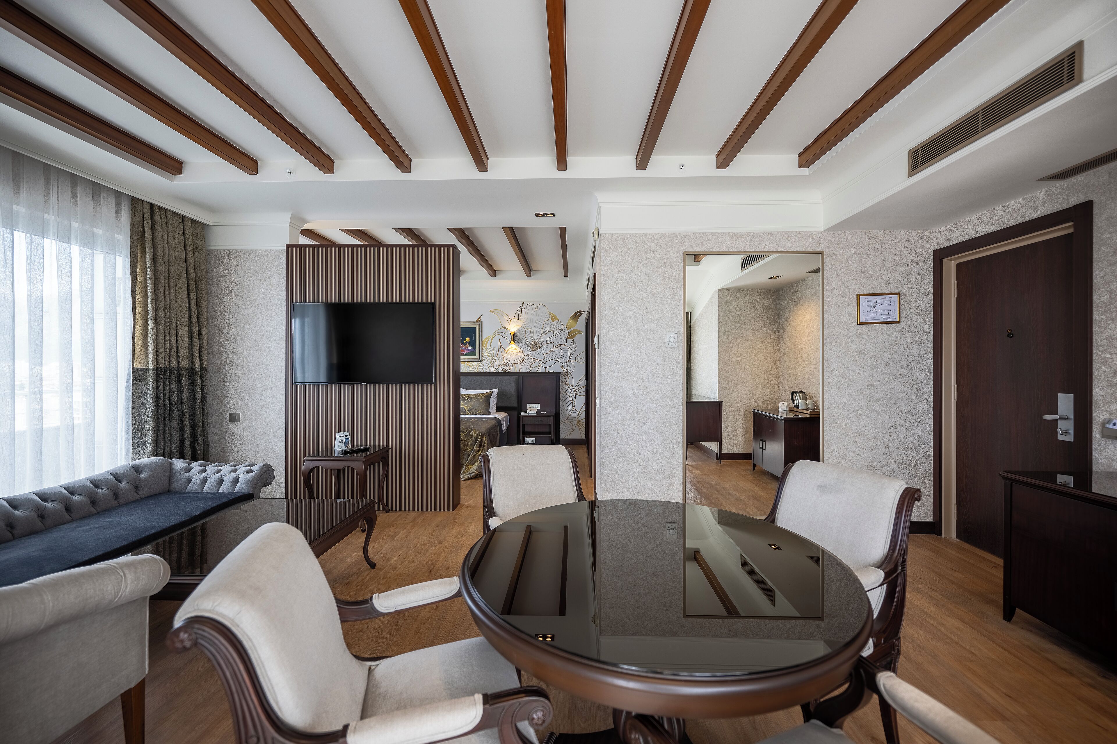 Una habitación de hotel moderna con una mesa redonda de cristal, sofás de cuero y techo de madera.