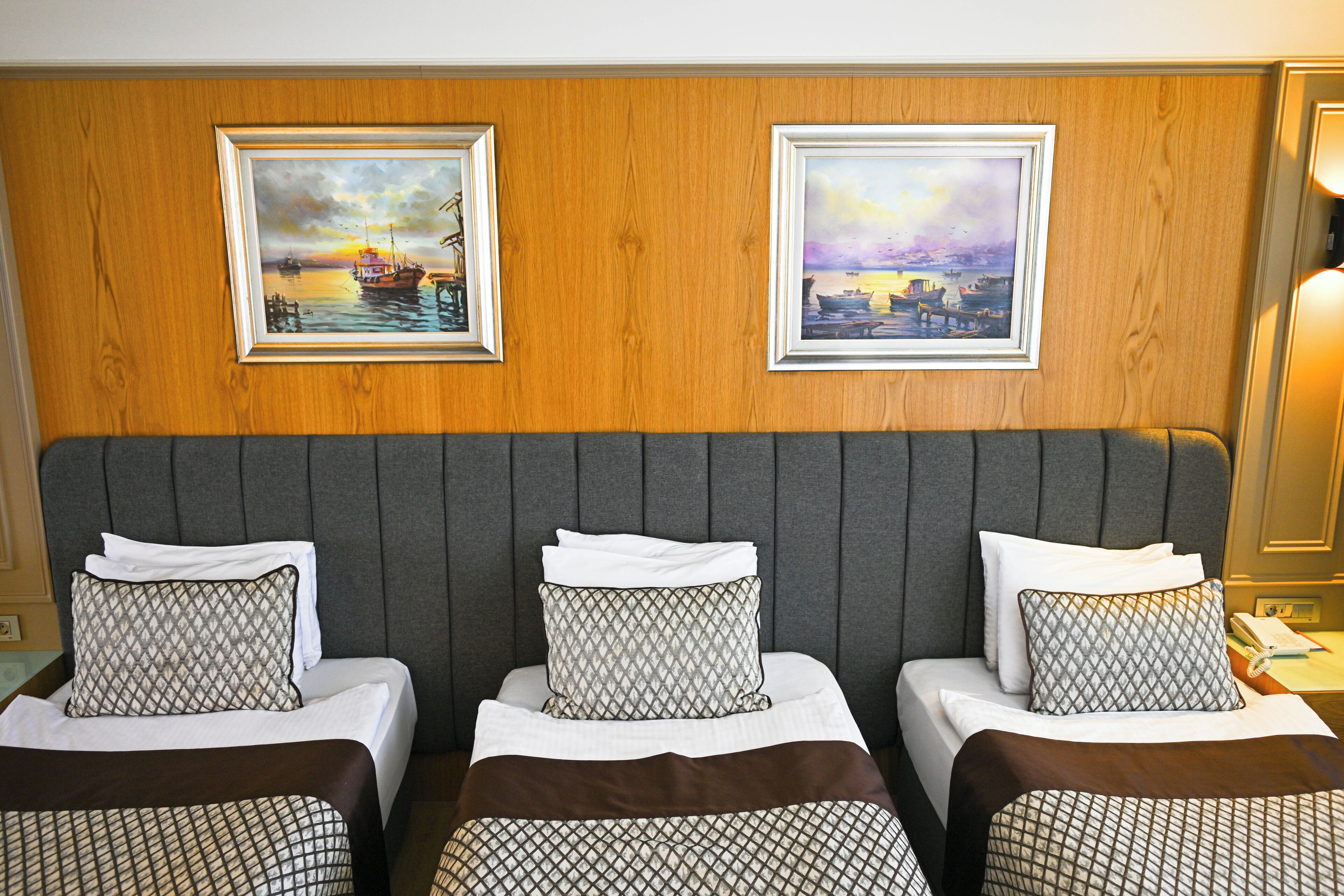 A hotel room with three beds, wooden paneling on the walls, and two framed paintings above the beds.