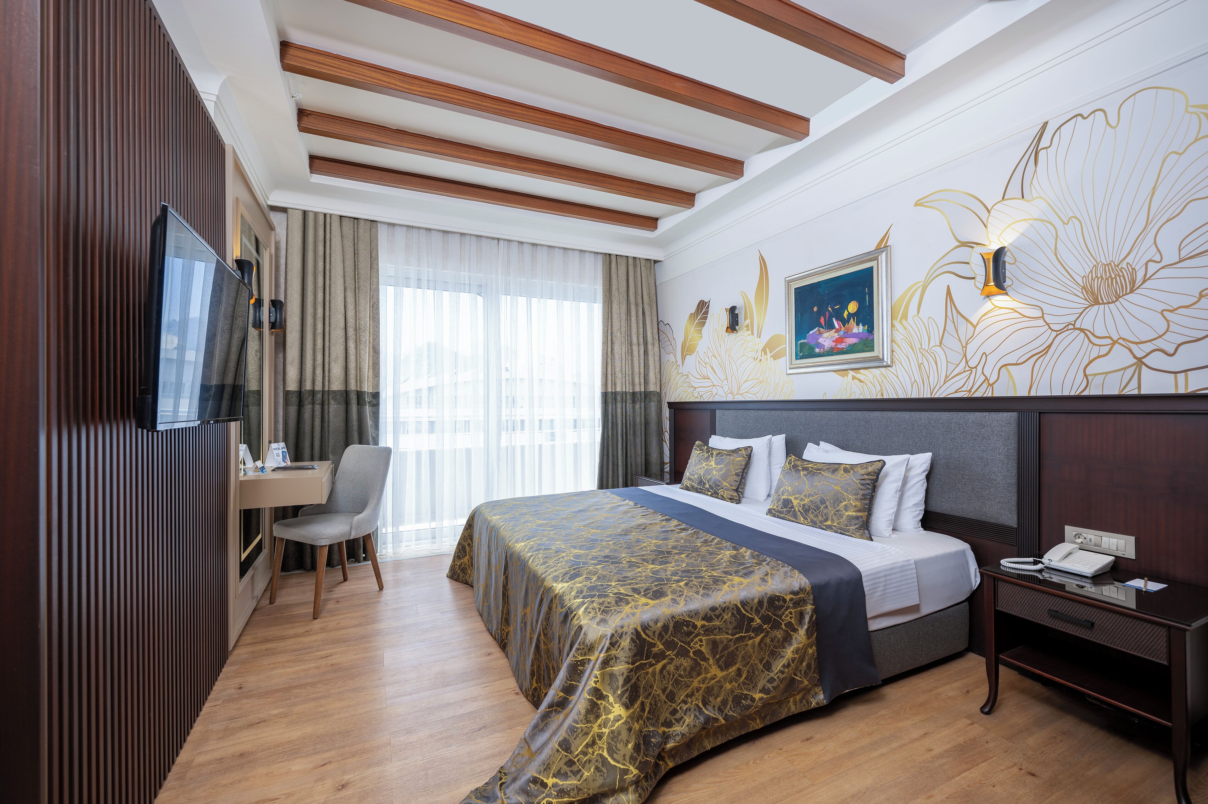 Hotelkamer met een bed, bureau, stoel, televisie en een wand met bloemenmotief.