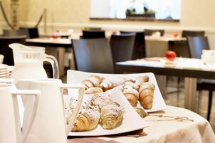 Colazione con croissant e un boccale di latte su un tavolo, con sedie e una finestra sullo sfondo.